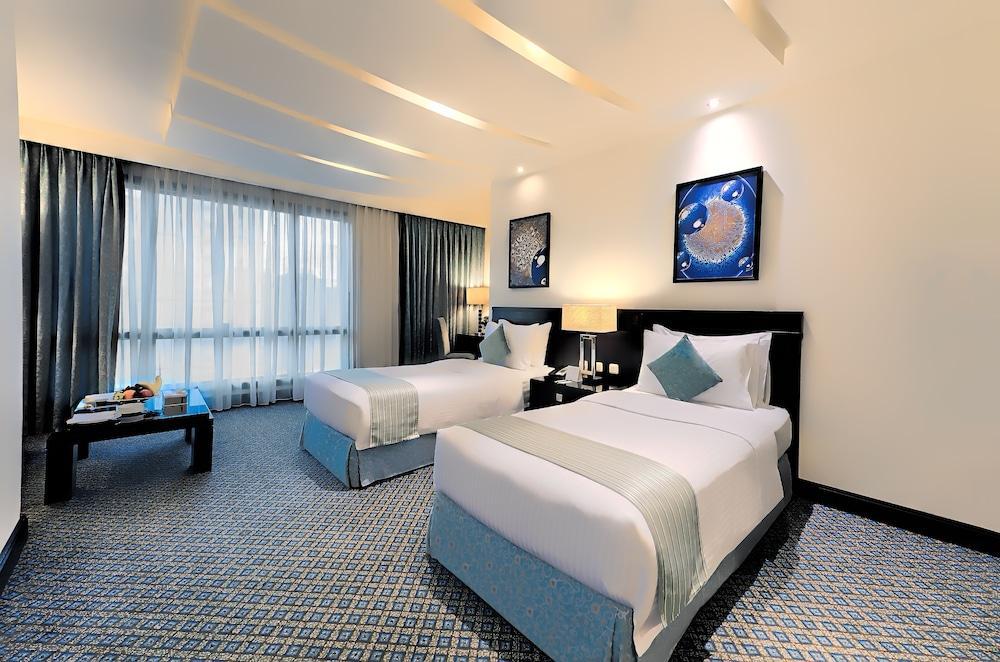 อัลคูฟราน ซาฟวะฮ์ โฮเต็ล มักกะฮ์ Hotel Mecca ภายนอก รูปภาพ The photo shows a hotel room with two twin beds. The beds are neatly made with white linens and light blue accents. There are decorative pillows on each bed. A black bedside table with lamps is situated between the beds. On the wall, there are two fr