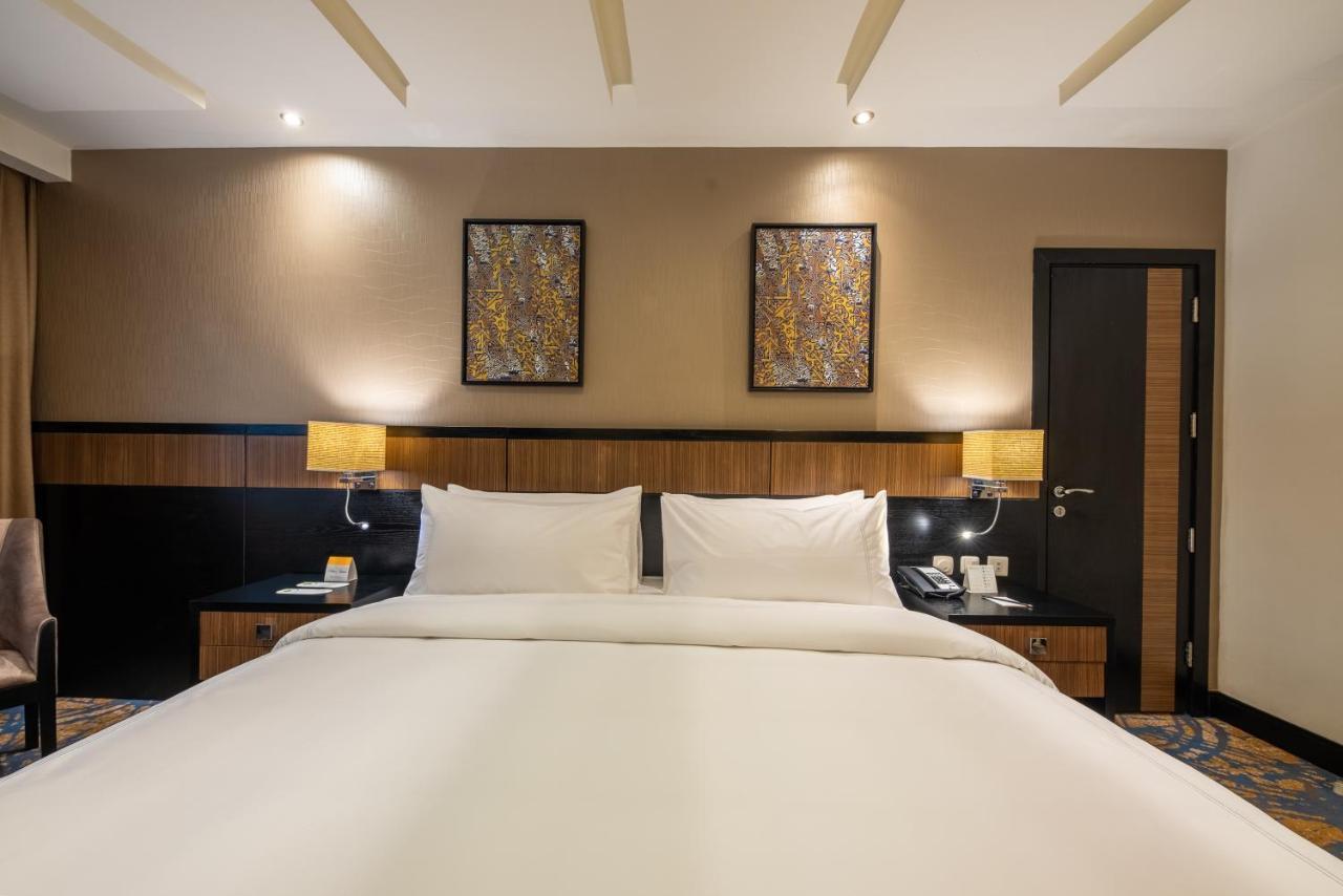 อัลคูฟราน ซาฟวะฮ์ โฮเต็ล มักกะฮ์ Hotel Mecca ภายนอก รูปภาพ The photo shows a hotel room featuring a large bed with white linens and two pillows. The background includes wooden elements, with bedside lamps on either side of the bed. Above the bed, there are two decorative wall art pieces. A dark-colored door 