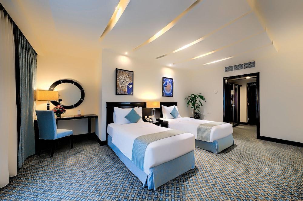 อัลคูฟราน ซาฟวะฮ์ โฮเต็ล มักกะฮ์ Hotel Mecca ภายนอก รูปภาพ The photo shows a modern hotel room featuring two single beds with light blue accents. There is a decorative piece of artwork on the wall above each bed. A round mirror is also hanging on the wall, complemented by a stylish lamp on a wooden bedside t