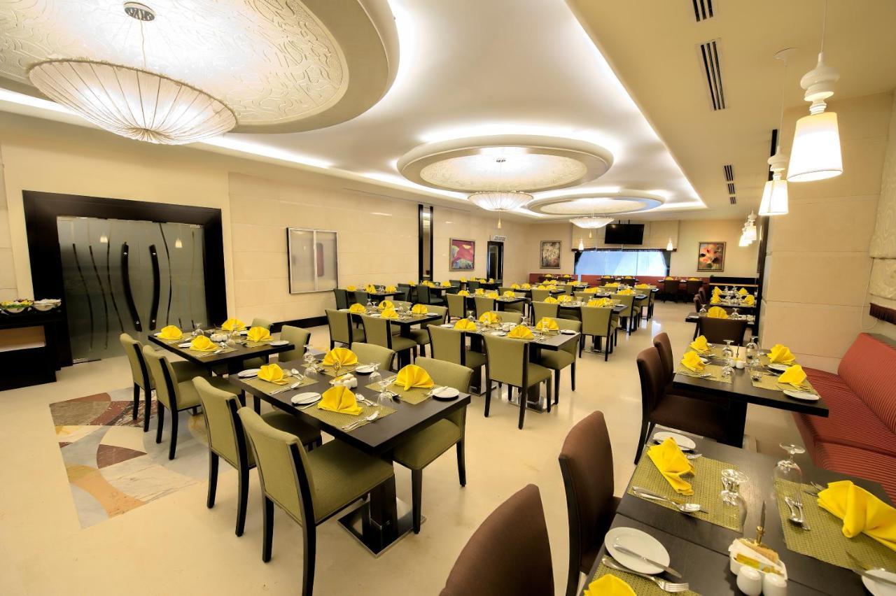 อัลคูฟราน ซาฟวะฮ์ โฮเต็ล มักกะฮ์ Hotel Mecca ภายนอก รูปภาพ The photo shows the interior of a modern restaurant. The space features neatly arranged tables with dark wooden surfaces and green chairs. Each table is set with yellow napkins, silverware, and glassware, suggesting a prepared dining atmosphere. The 