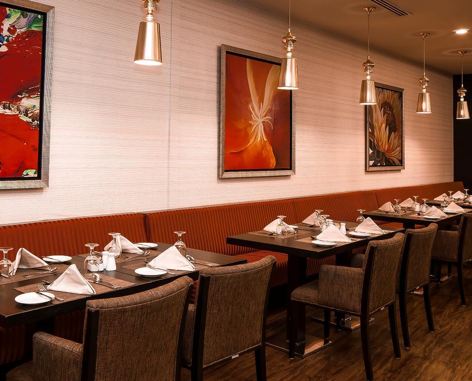 อัลคูฟราน ซาฟวะฮ์ โฮเต็ล มักกะฮ์ Hotel Mecca ภายนอก รูปภาพ The photo shows the interior of a restaurant. There are several tables set with white tablecloths, neatly folded napkins, and glassware. The walls are decorated with colorful artwork, including abstract paintings. The lighting is ambient, provided by