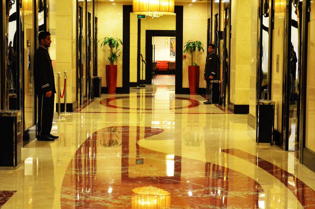 อัลคูฟราน ซาฟวะฮ์ โฮเต็ล มักกะฮ์ Hotel Mecca ภายนอก รูปภาพ The photo shows an elegant hallway in a building, likely a hotel or a high-end establishment. The floor is made of polished marble with a decorative pattern. There are two doormen or attendants standing on either side of the hallway, each dressed in 