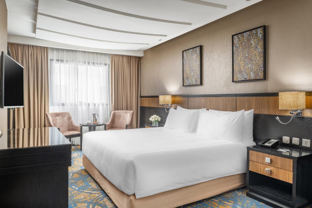 อัลคูฟราน ซาฟวะฮ์ โฮเต็ล มักกะฮ์ Hotel Mecca ภายนอก รูปภาพ The photo shows a modern hotel room featuring a spacious layout. In the center, there is a large bed with white linens. To the side, there are two upholstered chairs and a small table, creating a cozy sitting area. The room is decorated with stylish 