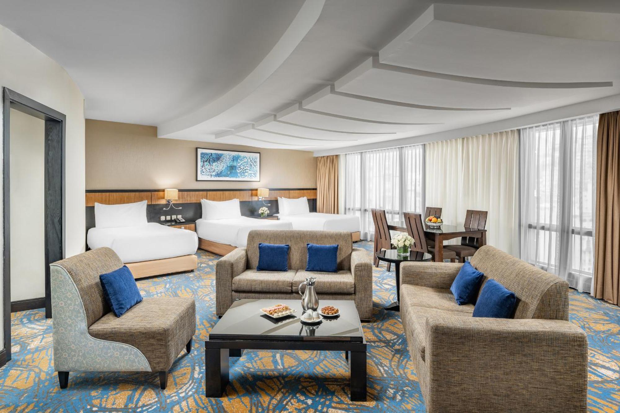 อัลคูฟราน ซาฟวะฮ์ โฮเต็ล มักกะฮ์ Hotel Mecca ภายนอก รูปภาพ The photo shows a spacious and elegantly designed hotel room. It features a cozy seating area with a coffee table surrounded by armchairs and a couch, adorned with blue cushions. In the background, there are two beds with white linens, suggesting a c